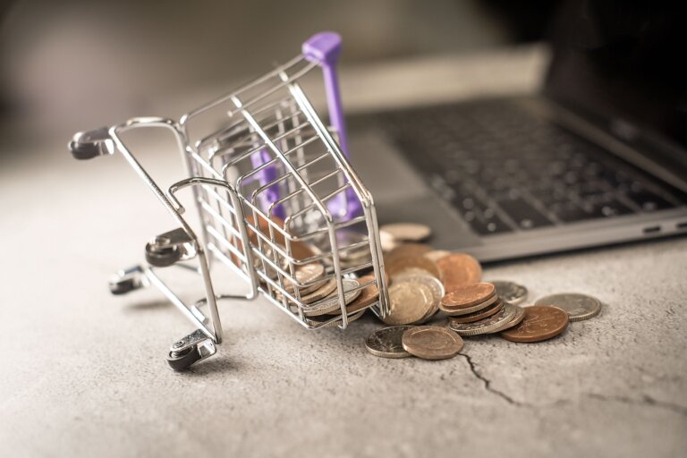 Miniature shopping cart with coins beside a laptop - WordPress.com Commerce vs self-hosted WooCommerce